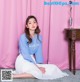 A woman sitting on the floor in front of a pink curtain.