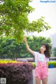 A woman in pink overalls pointing at a tree.