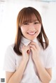 A woman in a white shirt is smiling and adjusting her tie.