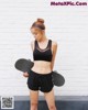 A woman holding a skateboard in front of a white brick wall.