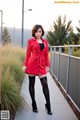 A woman in a red coat and black stockings posing for a picture.