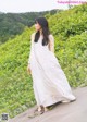 A woman in a long white dress standing on a dirt road.