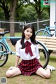 A woman in a school uniform sitting on the ground next to a bike.