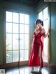 A woman in a red dress standing in front of a window.