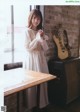 A woman standing in front of a window next to a guitar.