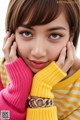 A woman wearing a yellow and pink sweater and a gold bracelet.