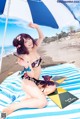 A woman in a bikini sitting on a beach under an umbrella.