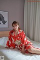 A woman in a red kimono sitting on a bed.