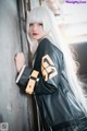 A woman with long white hair leaning against a wall.